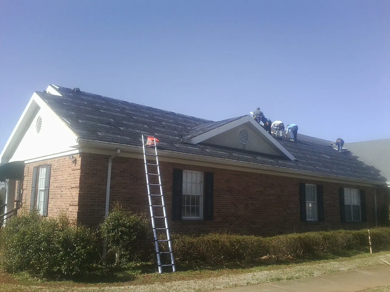 Crew tearing shingles off a brick ranch roof with a ladder set — Metal Roof Repair work by our crew in Russia