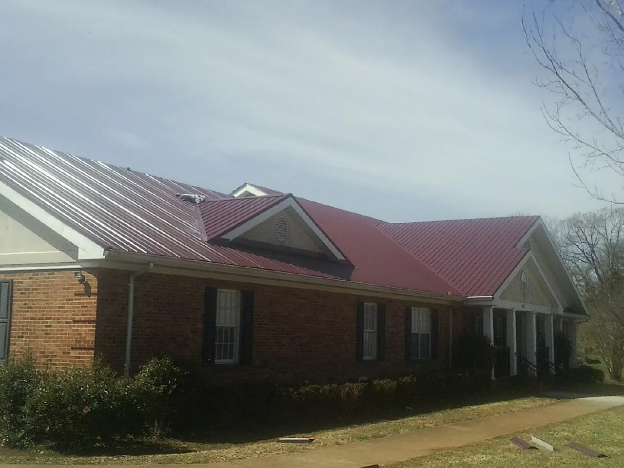 Red metal roof with gabled entries on a long brick building, from a Hail Damage Roof Repair job in Russia