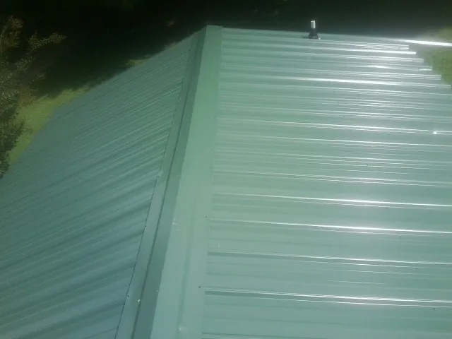 New green metal panels meeting at the ridge of a roof — Flat Roof Repair work by our crew in Russia