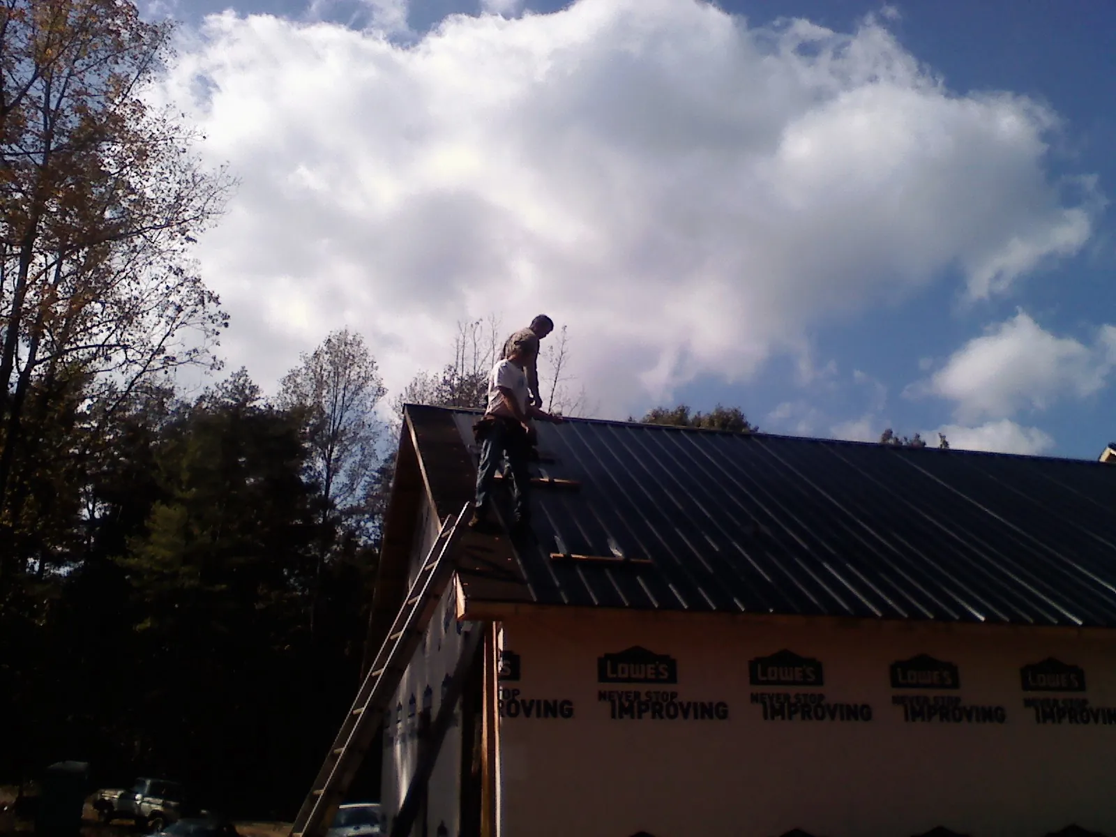 Roofer fastening dark metal panels high against a cloudy sky, from a Roof Inspection job in Russia