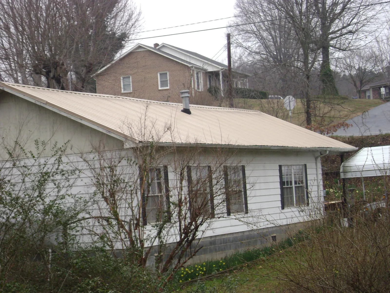 Tan metal roof on a white sided house set into a hillside — Commercial Roofing by Roofing Brothers in Russia