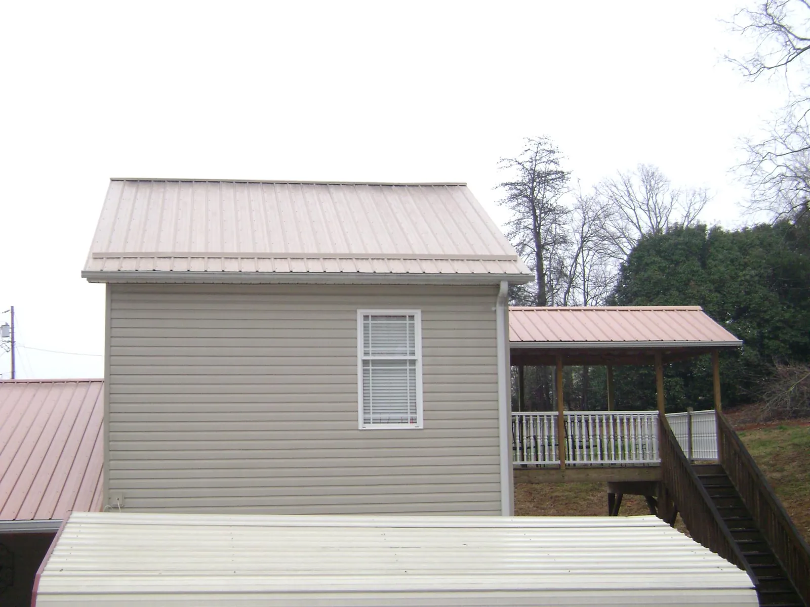Tan metal roofs on a two story addition and attached porch, from a Roof Replacement job in Russia